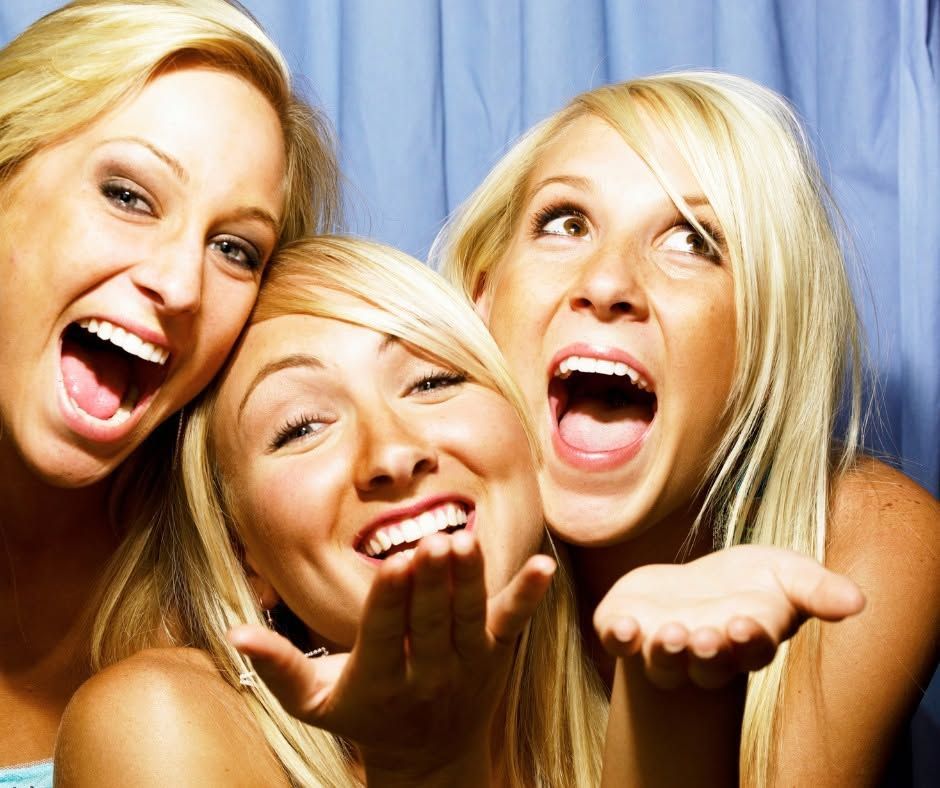 Three smiling people posing closely together against a blue curtain, making playful faces