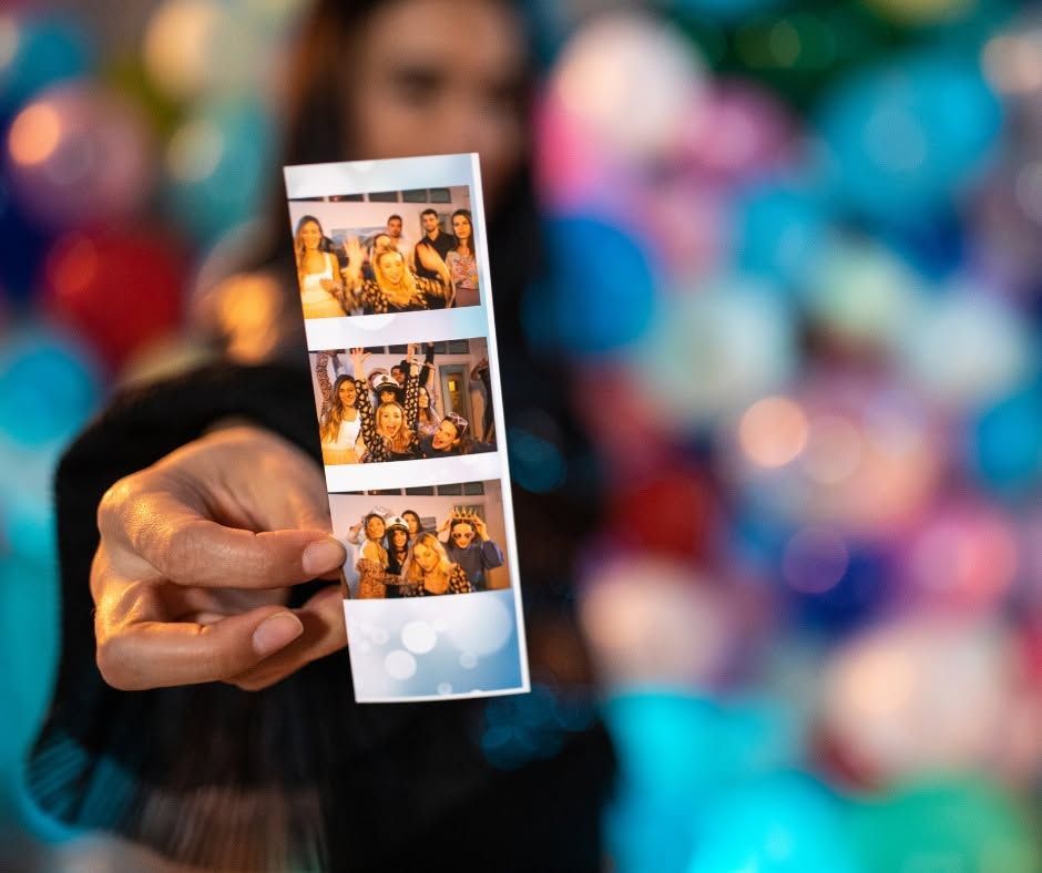 Hand holding a strip of four photo booth prints against a colorful blurred background