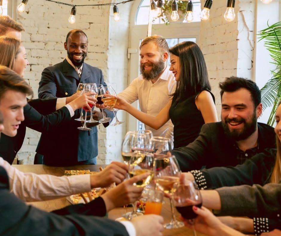 Friends raising glasses in a cozy restaurant, smiling around a dinner table with warm lights.