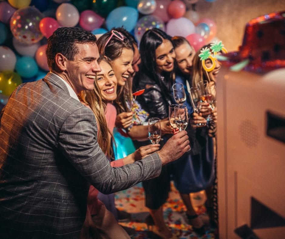 Friends toasting drinks at a festive birthday party with balloons and a cake