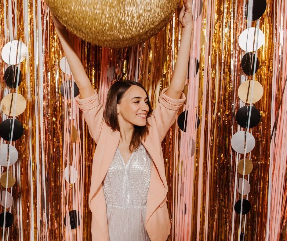 Woman in a sparkly dress with raised arms in a gold and pink party backdrop