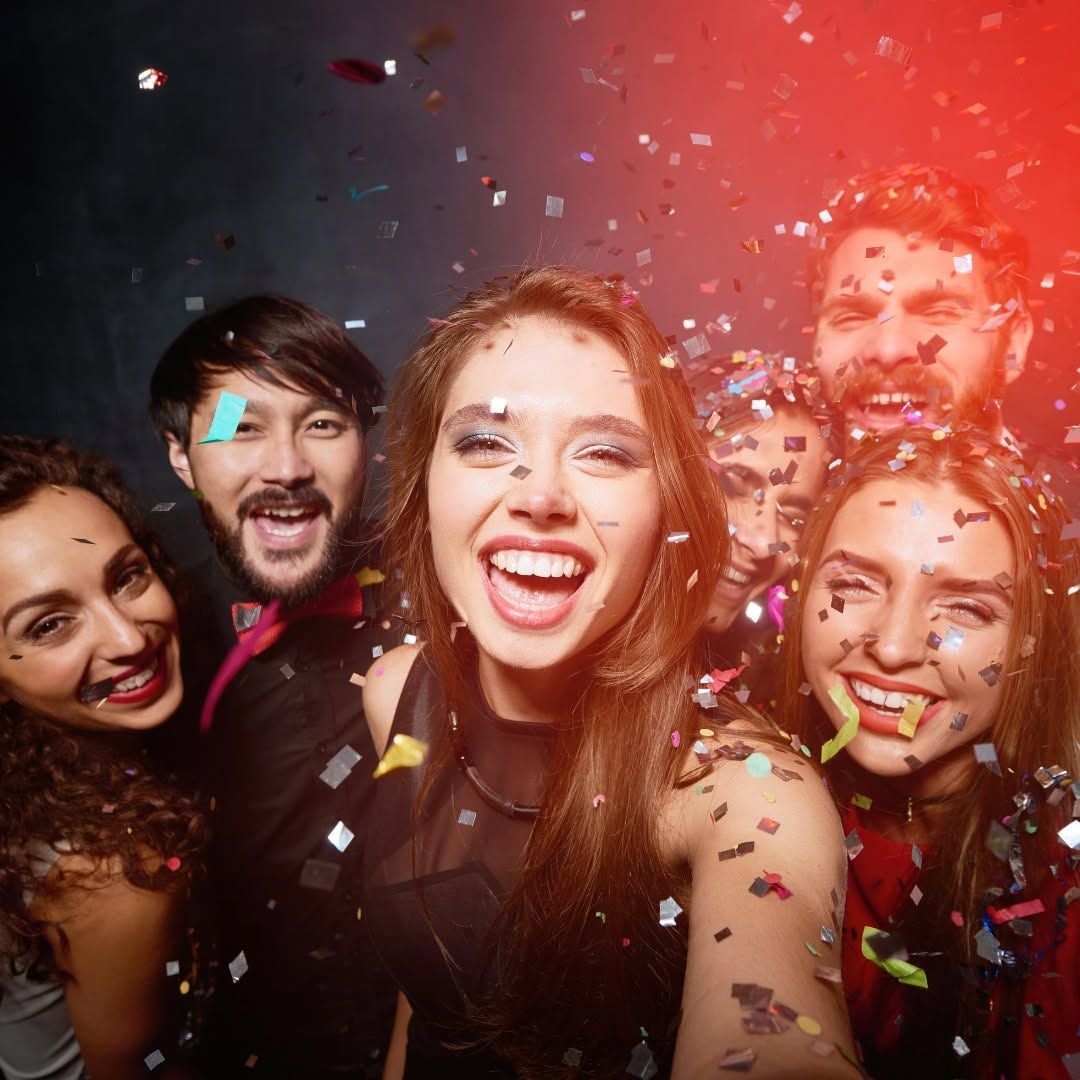 Group of friends smiling and laughing amid colorful confetti at a party