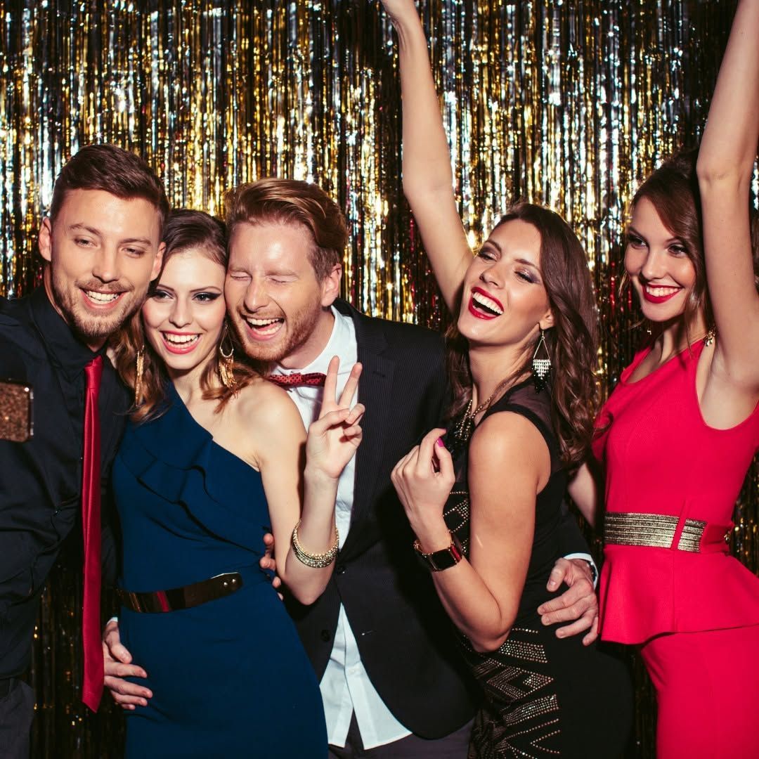 Five friends smiling and posing at a party in front of a gold tinsel backdrop
