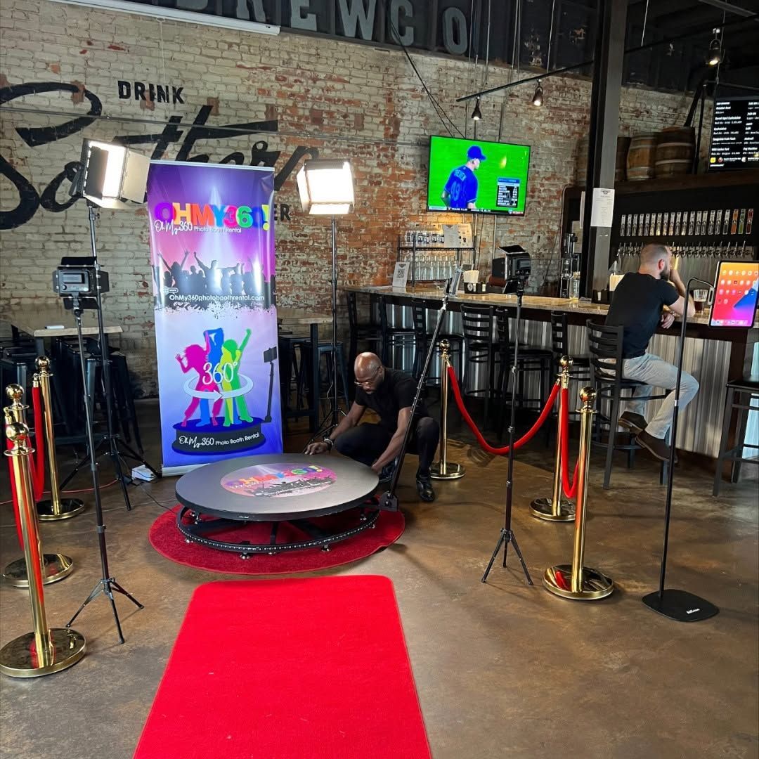 Event photo booth area with red carpet, colorful backdrop, lights, and a small stage in a restaurant/bar.