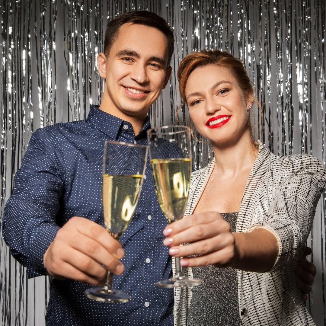 Two people toasting champagne flutes in front of a silver tinsel backdrop