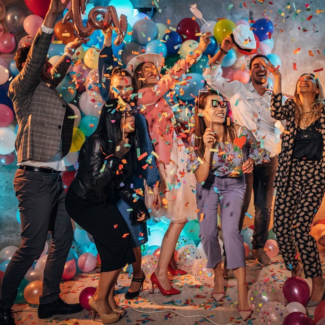 People celebrating at a balloon-filled party as confetti falls around them