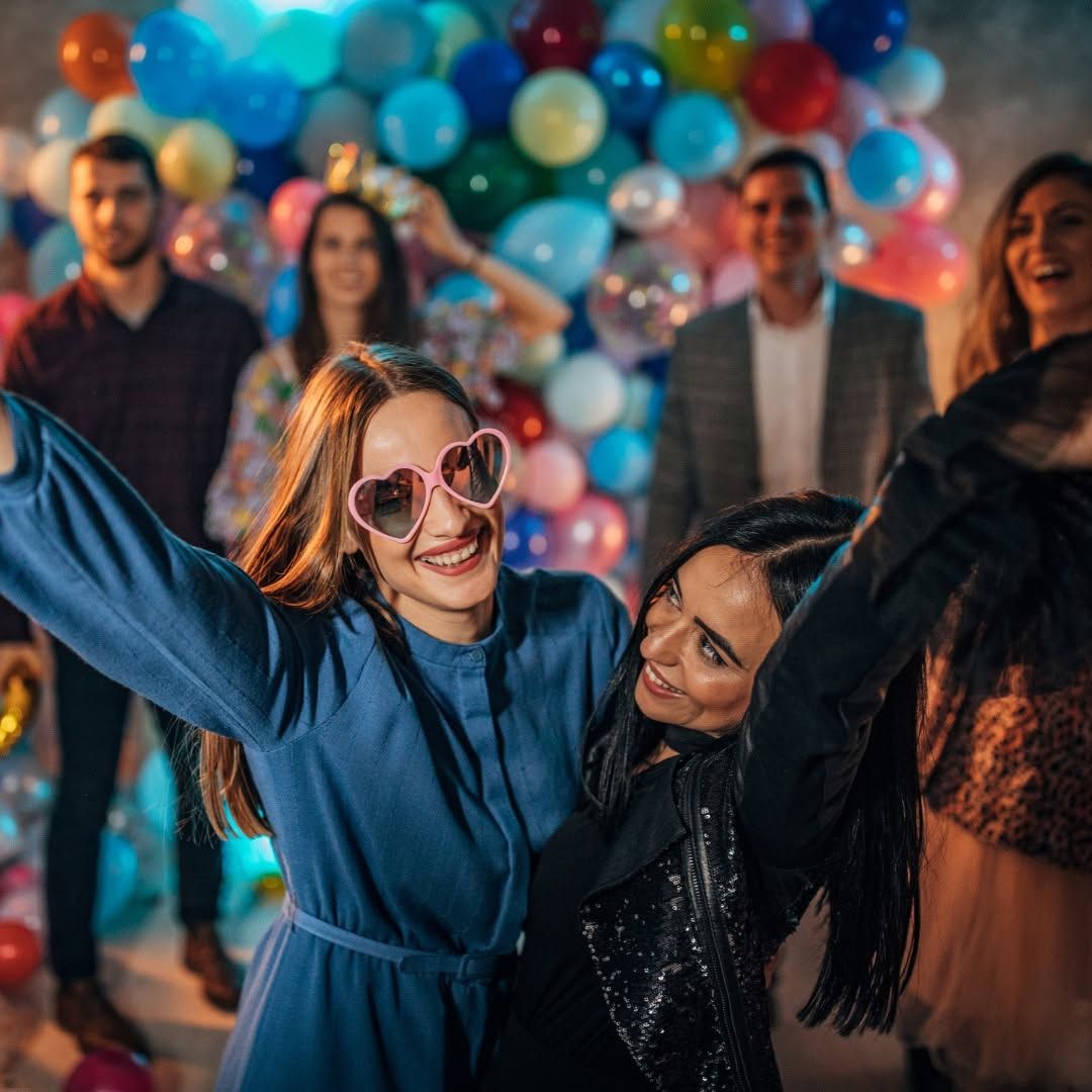 Women dancing at a colorful balloon party, smiling and posing with guests in the background