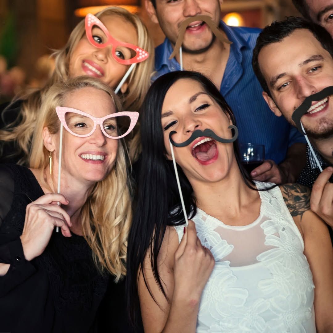 Four friends posing at a party wearing funny novelty glasses and mustaches, smiling and laughing