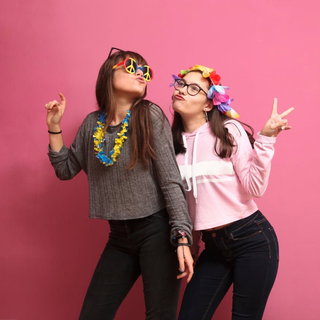 Two people posing playfully with colorful accessories against a pink background