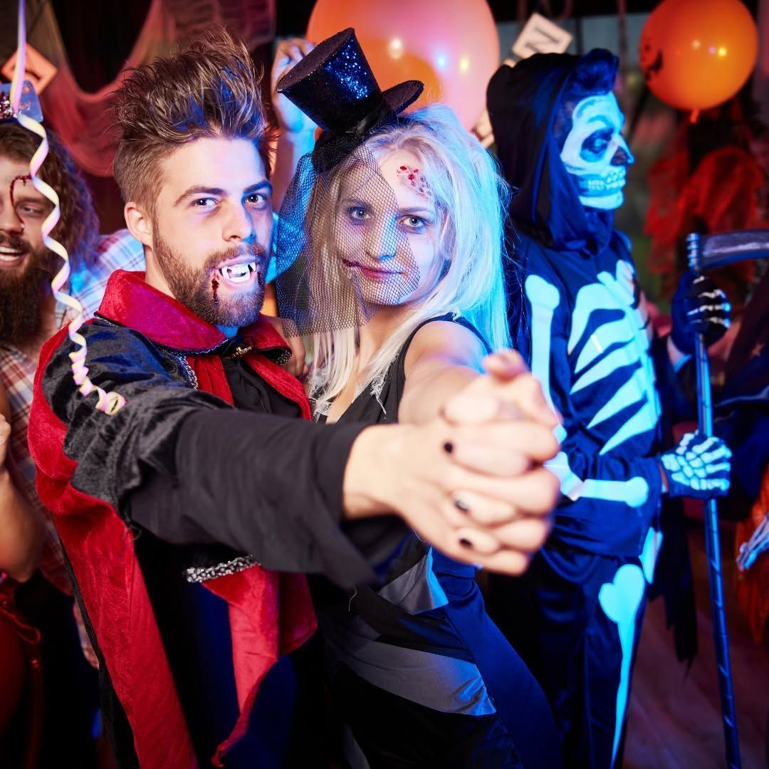 Costumed Halloween dancers posing at a party, with painted faces and balloons in the background