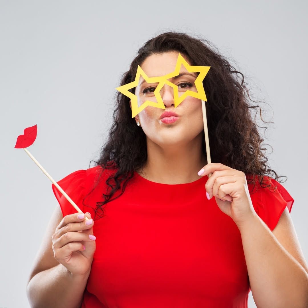 Person in red shirt wearing star-shaped glasses and holding a red lipstick prop, making a kissy face.
