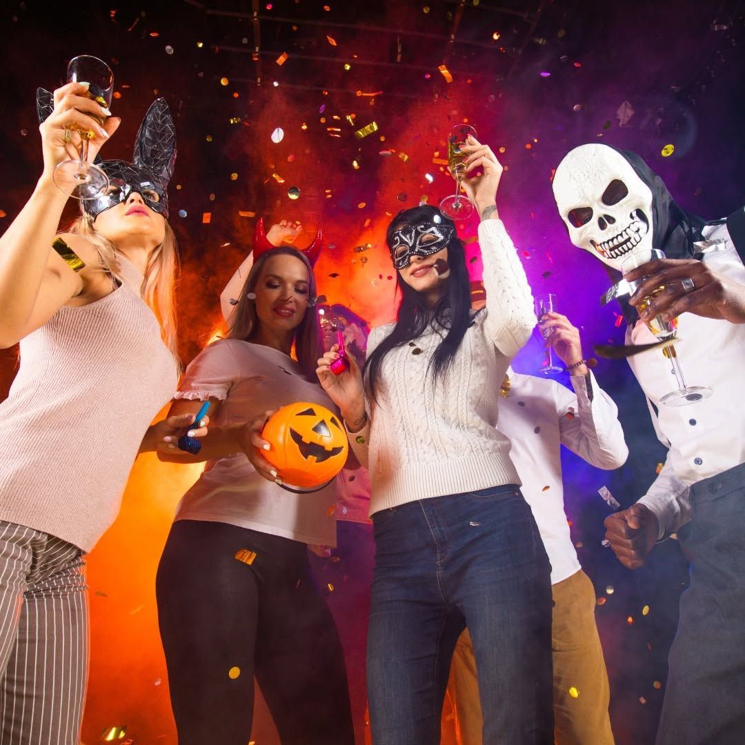 People in Halloween costumes dancing amid confetti, with a pumpkin bucket and skull mask.
