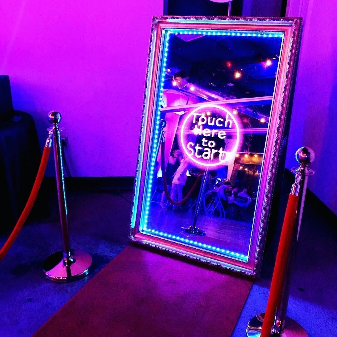 Neon-lit mirror sign reading “Touch here to Start” between velvet ropes