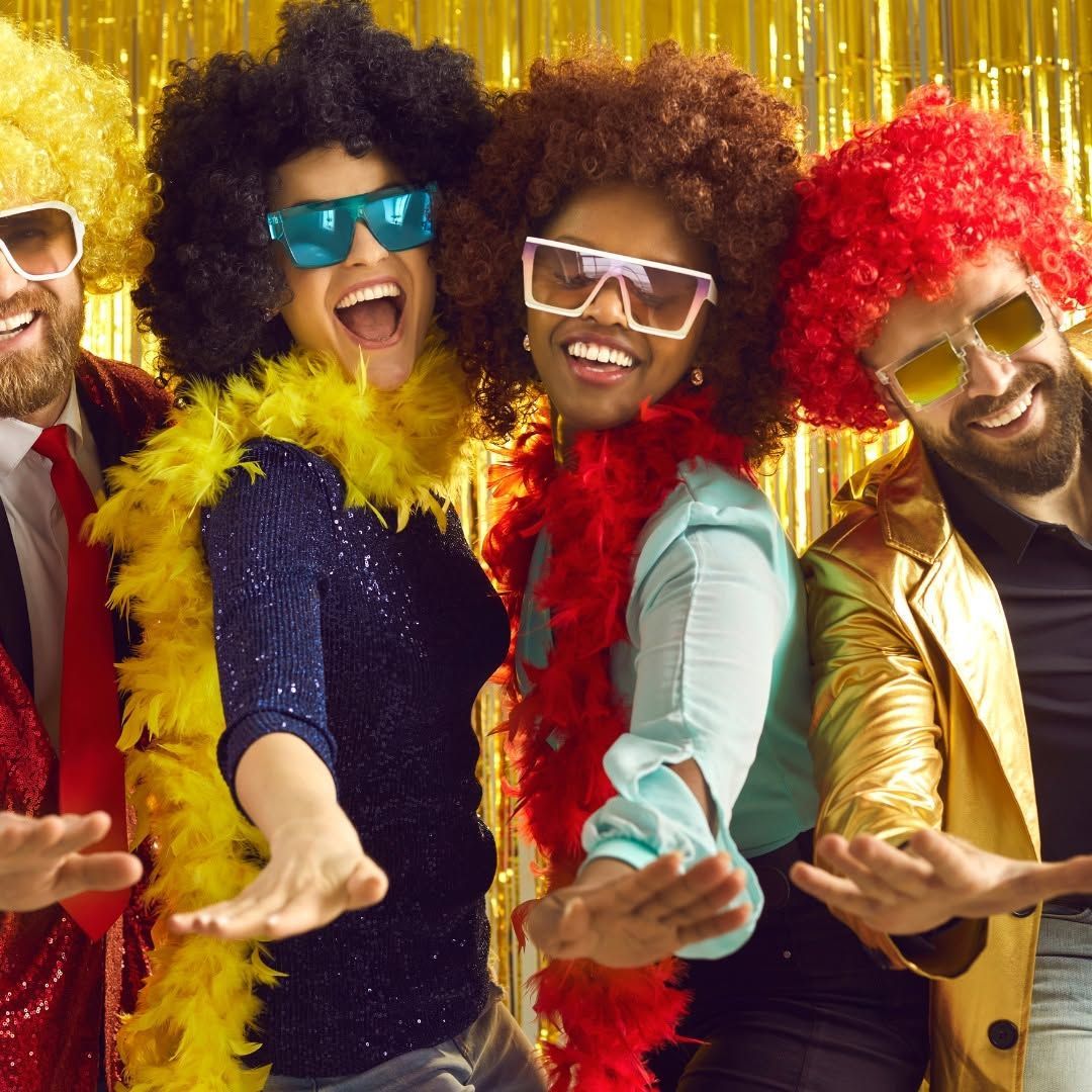Four smiling dancers in colorful retro outfits and sunglasses posing with outstretched hands against gold tinsel
