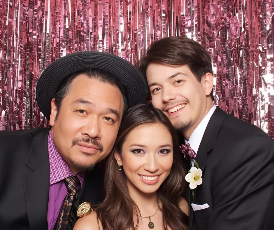 Three people posing in formal attire before a pink tinsel backdrop