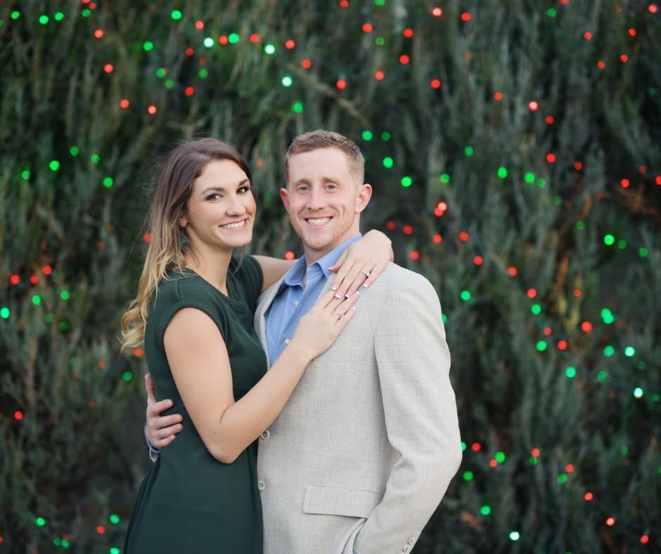 Couple posing together outdoors in formal wear, smiling in front of a twinkling lighted backdrop