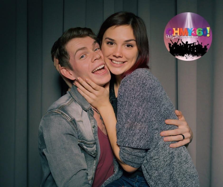 Two smiling people hugging, one holding the other’s face, against a dark striped background.