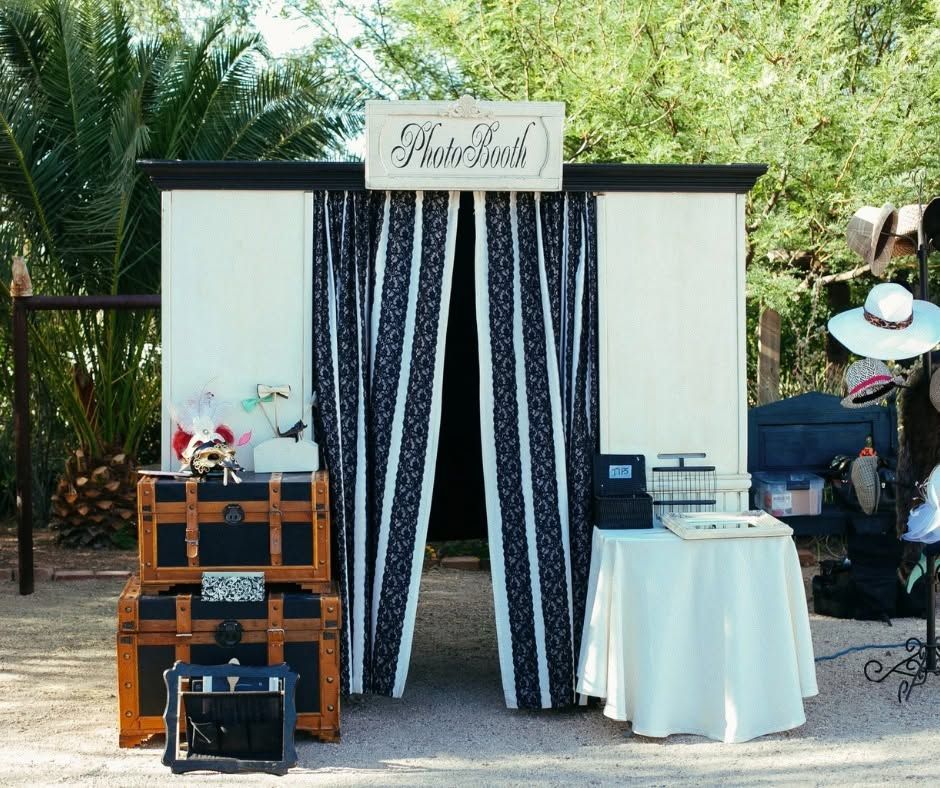 Rustic booth with black-and-white drapes, wooden crates, flowers, and a white table in an outdoor garden setting