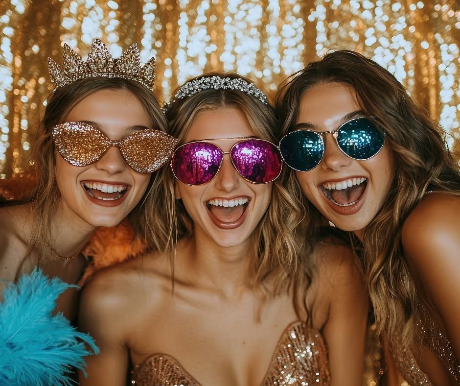 Three smiling people in sparkly party glasses and crowns posing at a festive celebration.