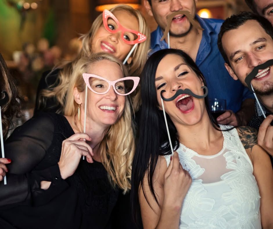 Four friends in costume glasses smiling and posing closely together at a party