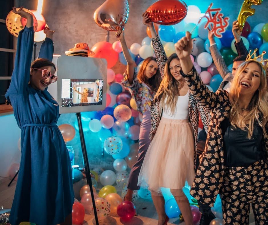 Three women celebrate in a balloon-filled room with raised arms and smiles