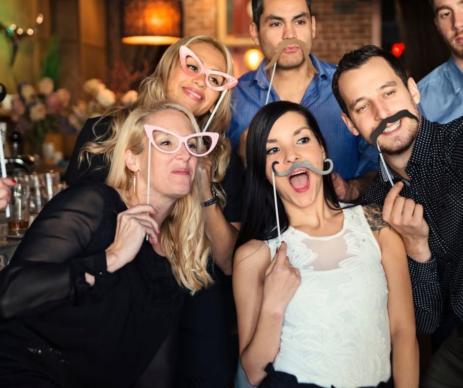 Five people posing playfully at a party, wearing novelty glasses and making funny faces at the camera.