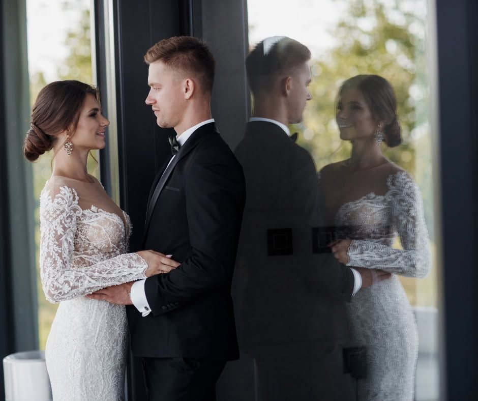 Bride and groom in wedding attire holding hands beside a reflective glass wall