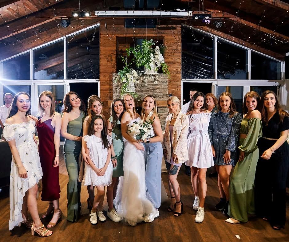 Group of women posing at a wedding reception in a rustic, wood-paneled venue with warm lights.