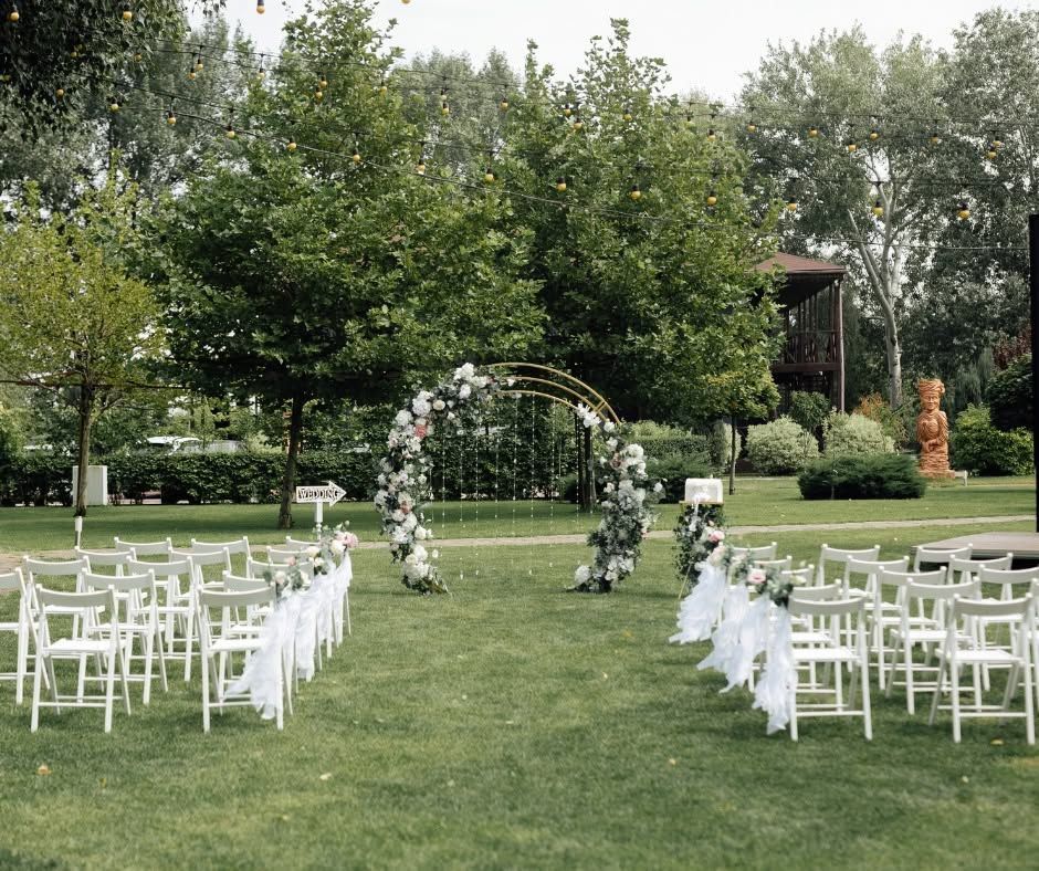 Outdoor wedding setup with white chairs, floral arch, and green lawn in a garden setting