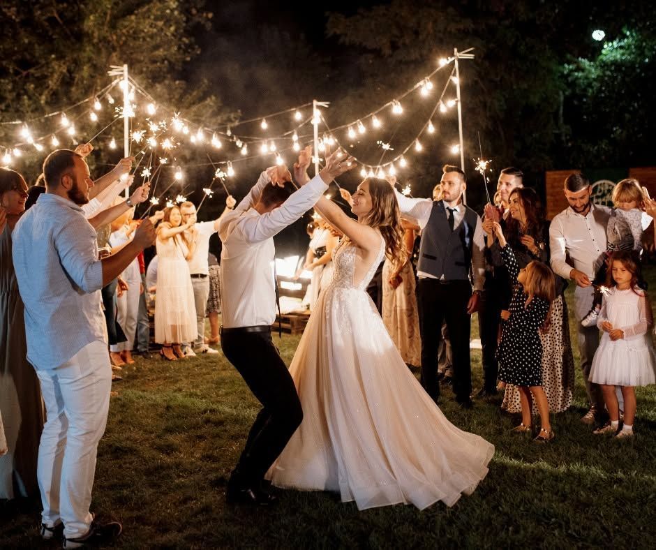 Couple dancing at an outdoor wedding reception under string lights, surrounded by applauding guests.