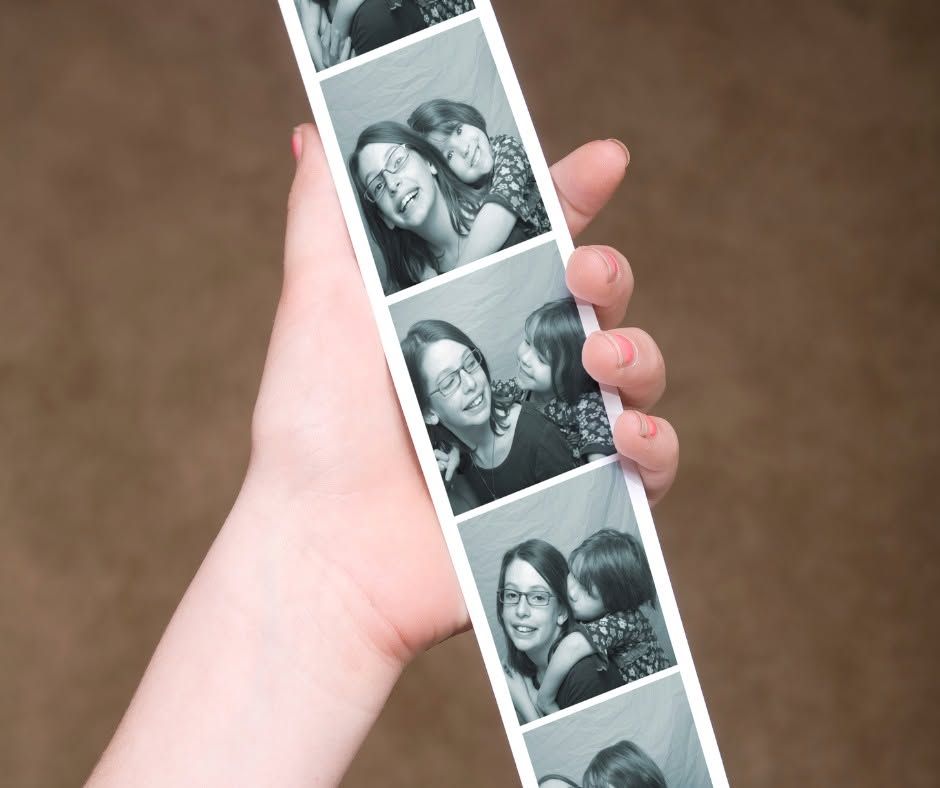 Hand holding a strip of black-and-white photo booth pictures showing two smiling people posing together