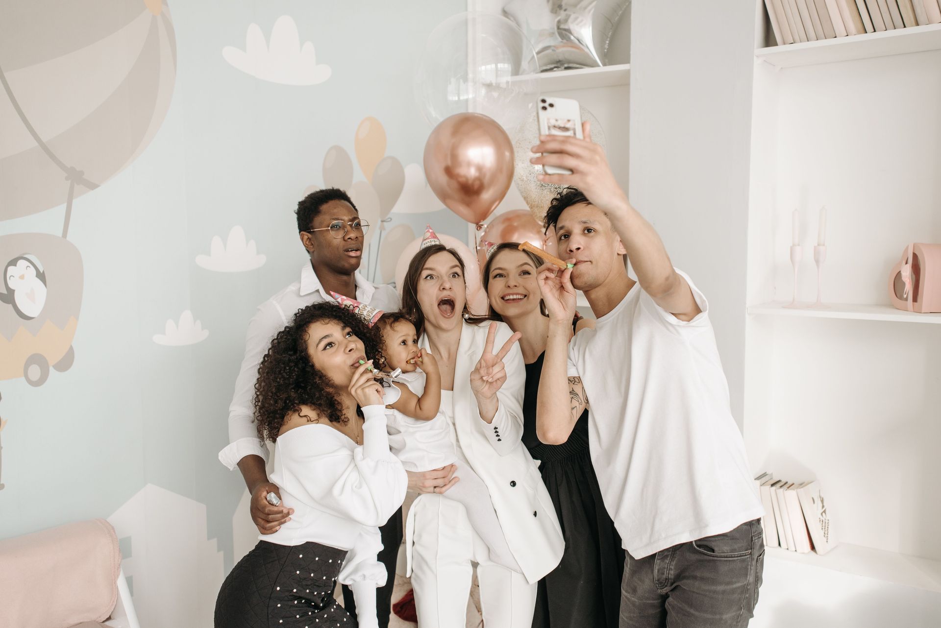 Friends smiling and posing for a selfie at a birthday party with white and rose-gold balloons