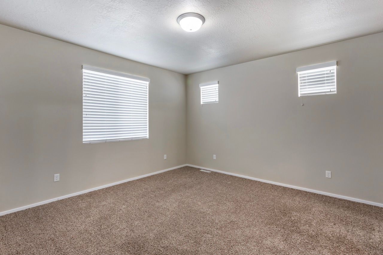 Empty beige-carpeted bedroom with three small windows and a ceiling light.