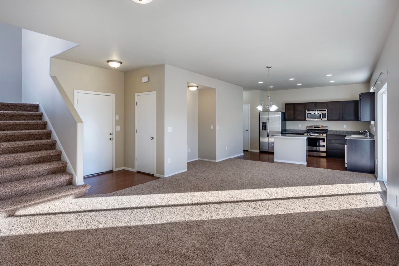 Open-concept living area with stairs on the left, entry doors, and a modern kitchen with stainless appliances.