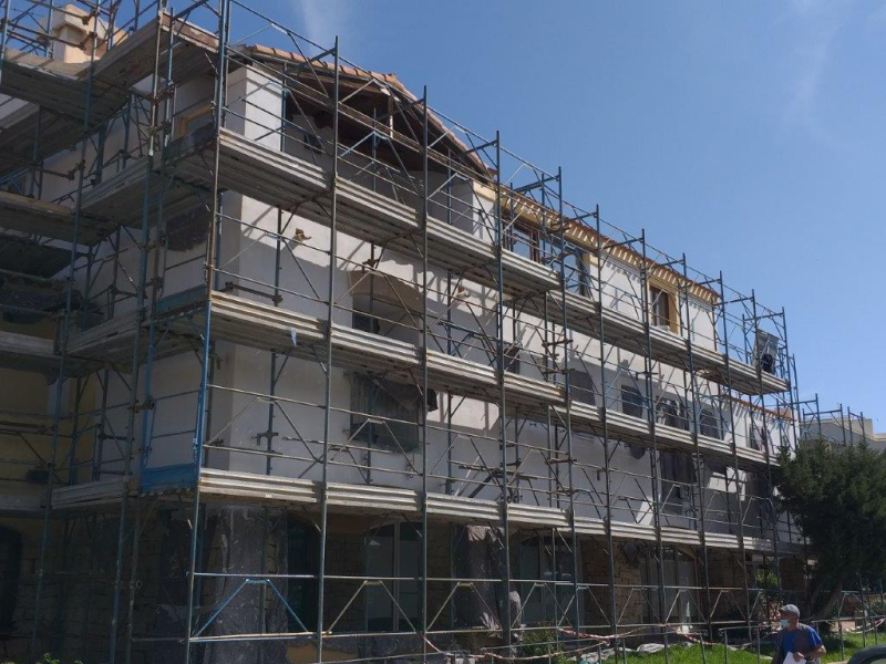Edificio in fase di ristrutturazione con impalcature, esterno bianco, cielo azzurro.