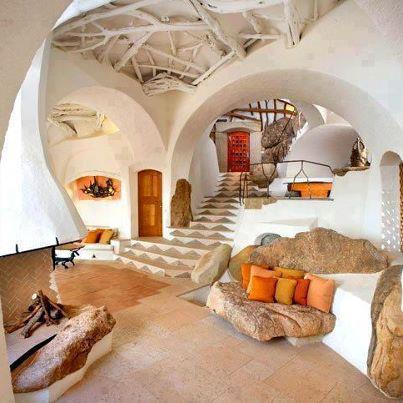 Interni in stile organico con soffitti a volta, formazioni rocciose, una scala e una porta rossa. Colori caldi.