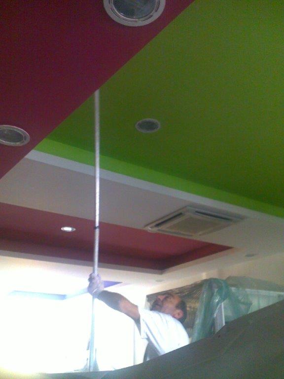 Persona che allunga un'asta verso un soffitto con pannelli rosa, verdi e bianchi.
