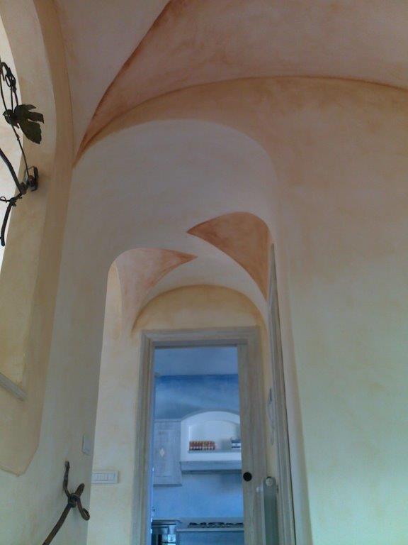 Corridoio ad arco con pareti e soffitto chiari, che conduce a una stanza blu attraverso una porta aperta.