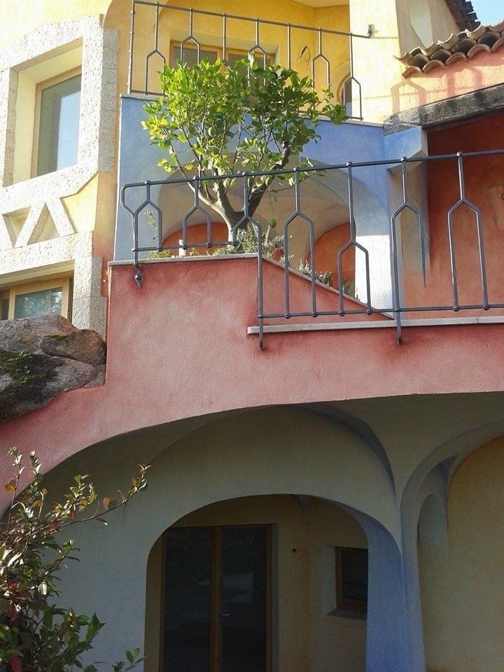 Edificio colorato con passaggi ad arco e un balcone con un piccolo albero; vista esterna.