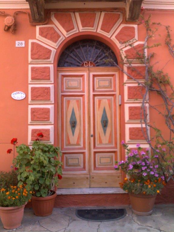 Porta rossa con parte superiore arcuata, circondata da dettagli in pietra e fiancheggiata da piante in vaso.