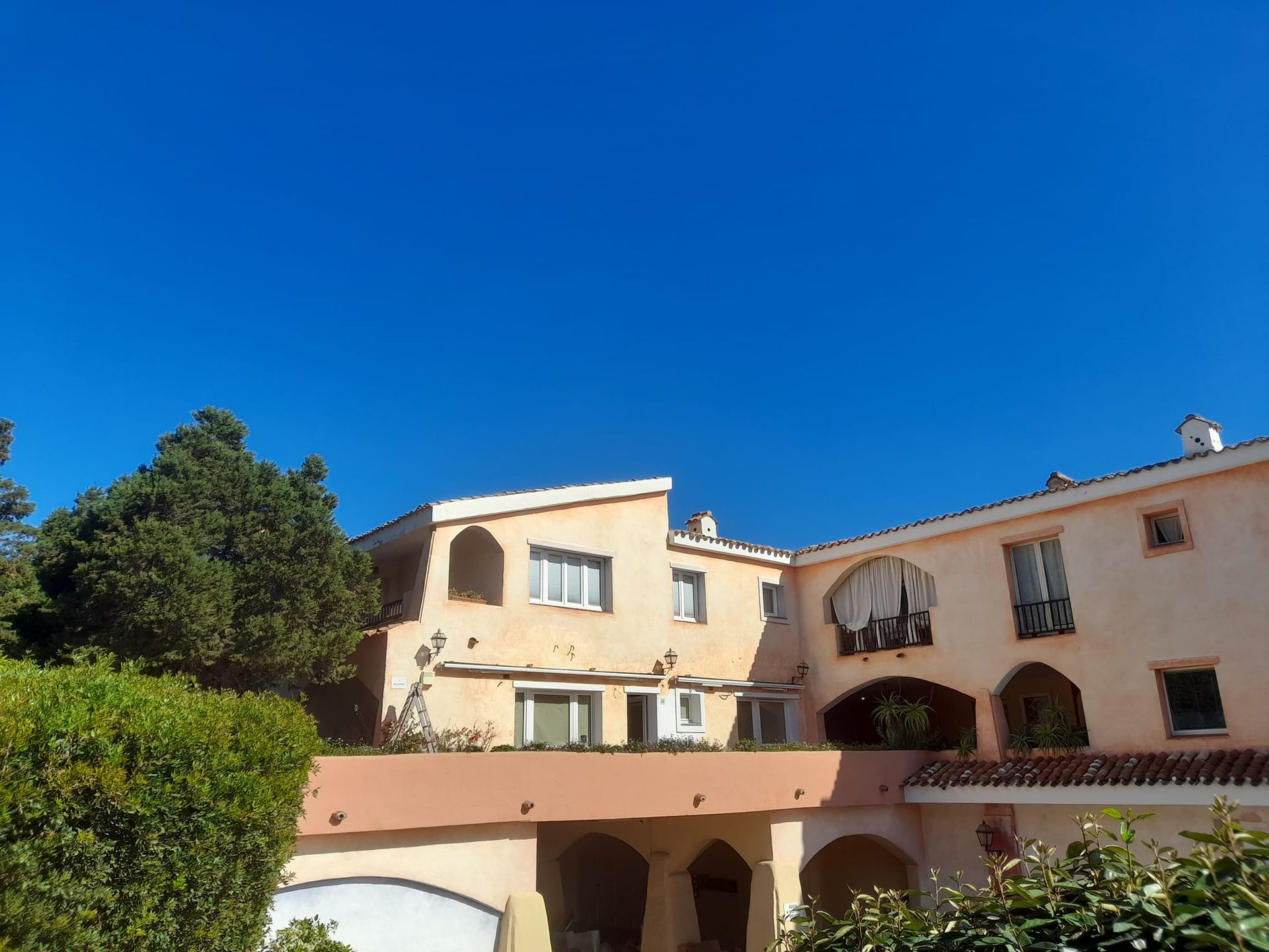 Edifici beige con porte ad arco, balconi e un cielo azzurro e terso.