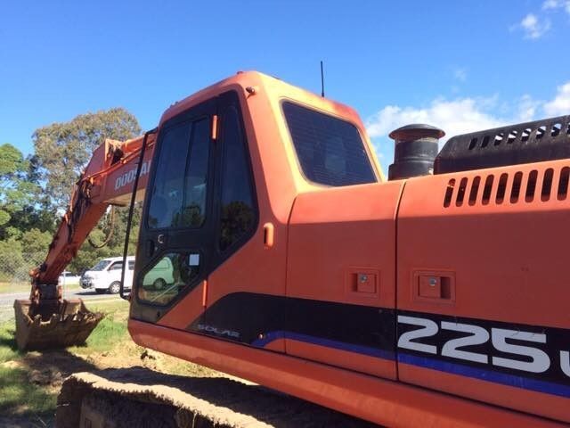Orange Doosan 225LC excavator on a construction site with a blue sky.