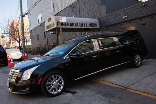 Black hearse parked at an angle beside a bakery storefront on a city street