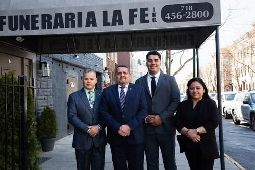 Four people in suits standing outside a funeral home storefront.