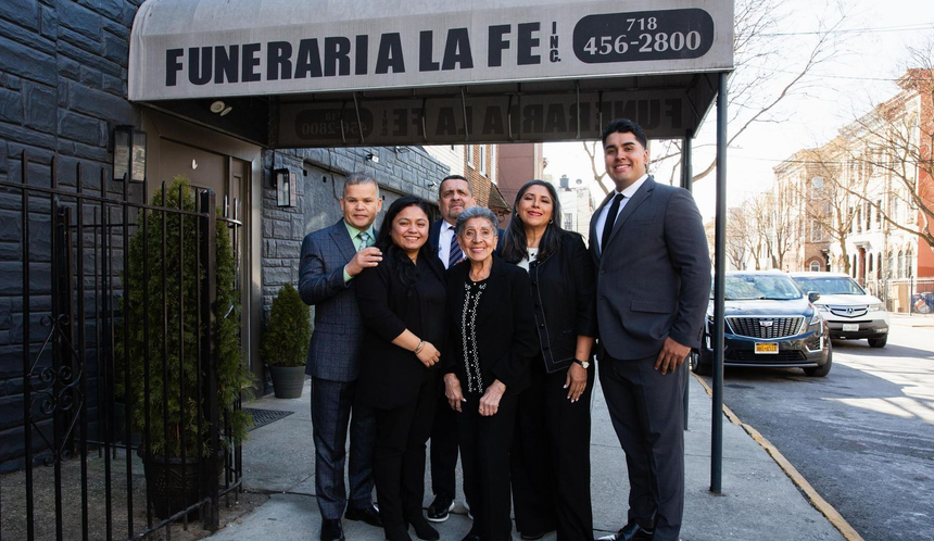 Five people standing outside Funeraria La Fe under the awning, smiling at the camera.