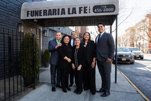 Group standing outside Funeraria La Fe funeral home on a city sidewalk.
