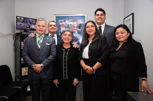 Five people in formal black attire posing together in an office.