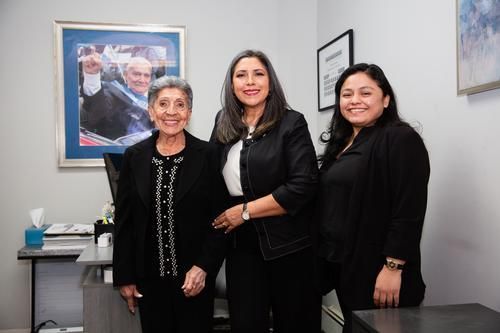 Three people standing together in an office, smiling in front of framed wall art.