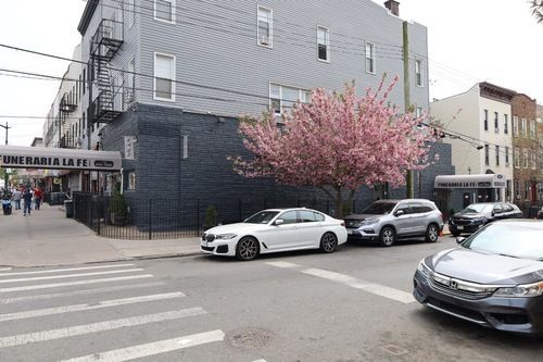 Street corner with parked cars, a pink flowering tree, and a funeral home sign on a gray building.