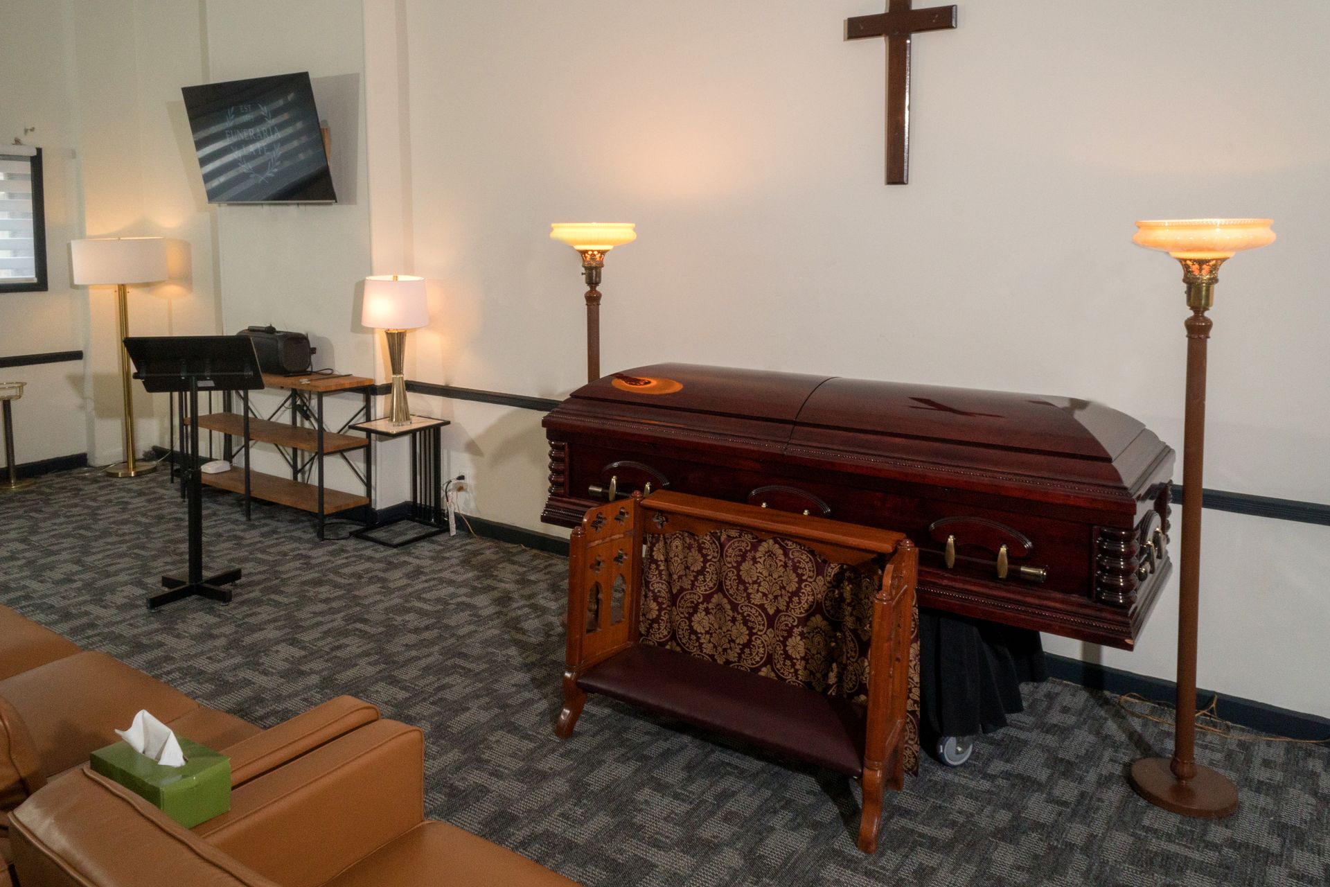 Small funeral chapel with a casket, cross, lamps, and memorial table.